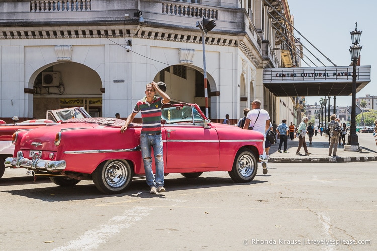 Man standing with a pink classic car with a theatre in the background.